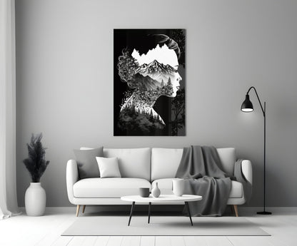 Black and white double-exposure glass art showing a woman's silhouette filled with a mountain landscape, displayed above a white sofa in a minimalist living room.