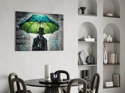 Glass wall art depicting a silhouetted figure holding a green and blue umbrella in rain, displayed above a dining table in a modern interior.