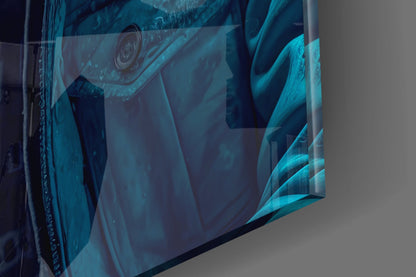 Close-up angled view of turquoise and dark blue glass wall art with abstract ape design, displayed against gray wall.