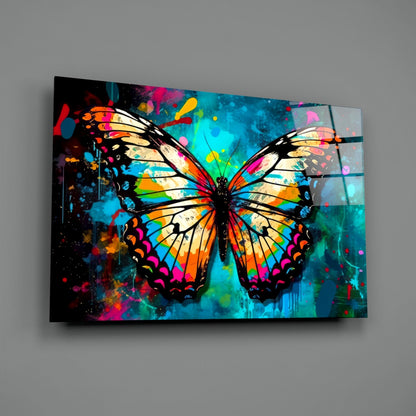 Colorful glass wall art panel displaying a vibrant butterfly with orange, yellow, blue, and pink wings against an abstract splattered background.