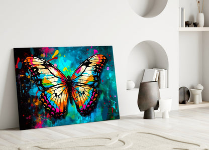 Colorful glass wall art featuring a vibrant butterfly with orange, yellow, blue, and pink wings displayed in a minimalist white room setting.