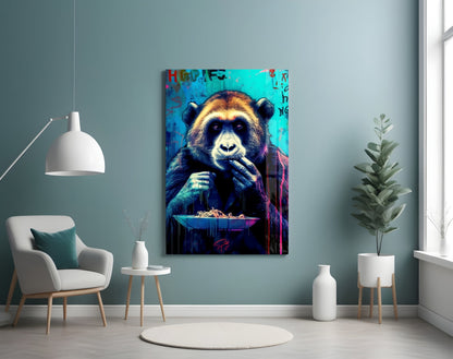 Vibrant glass wall art depicting a colorful chimp holding utensils over a plate against bright turquoise background, displayed in modern living room setting.