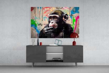Thinking Monkey glass wall art mounted above gray media console in modern living room setting with colorful graffiti background.