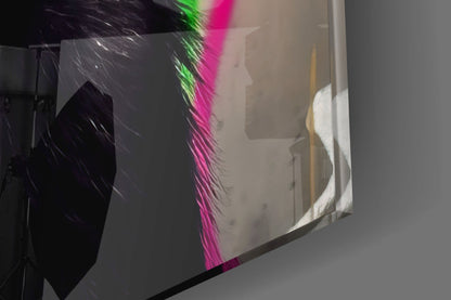Colorful feathered glass wall art with neon green and magenta plumage, photographed at an angle showing depth and light reflection.