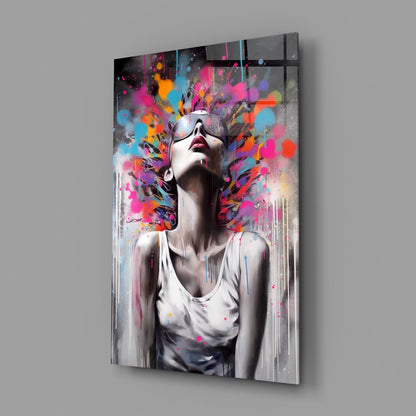 Modern glass wall art panel displaying a portrait of a woman wearing sunglasses with vibrant multicolored paint splatters exploding around her head against a white background.