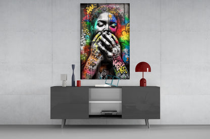 Vertical glass wall art displaying a grayscale face with colorful graffiti and abstract elements surrounding it, mounted above a dark console table.