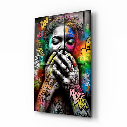 Angled three-quarter view of glass wall art featuring monochrome face with colorful graffiti, rainbow gradient background, and tattooed hands.