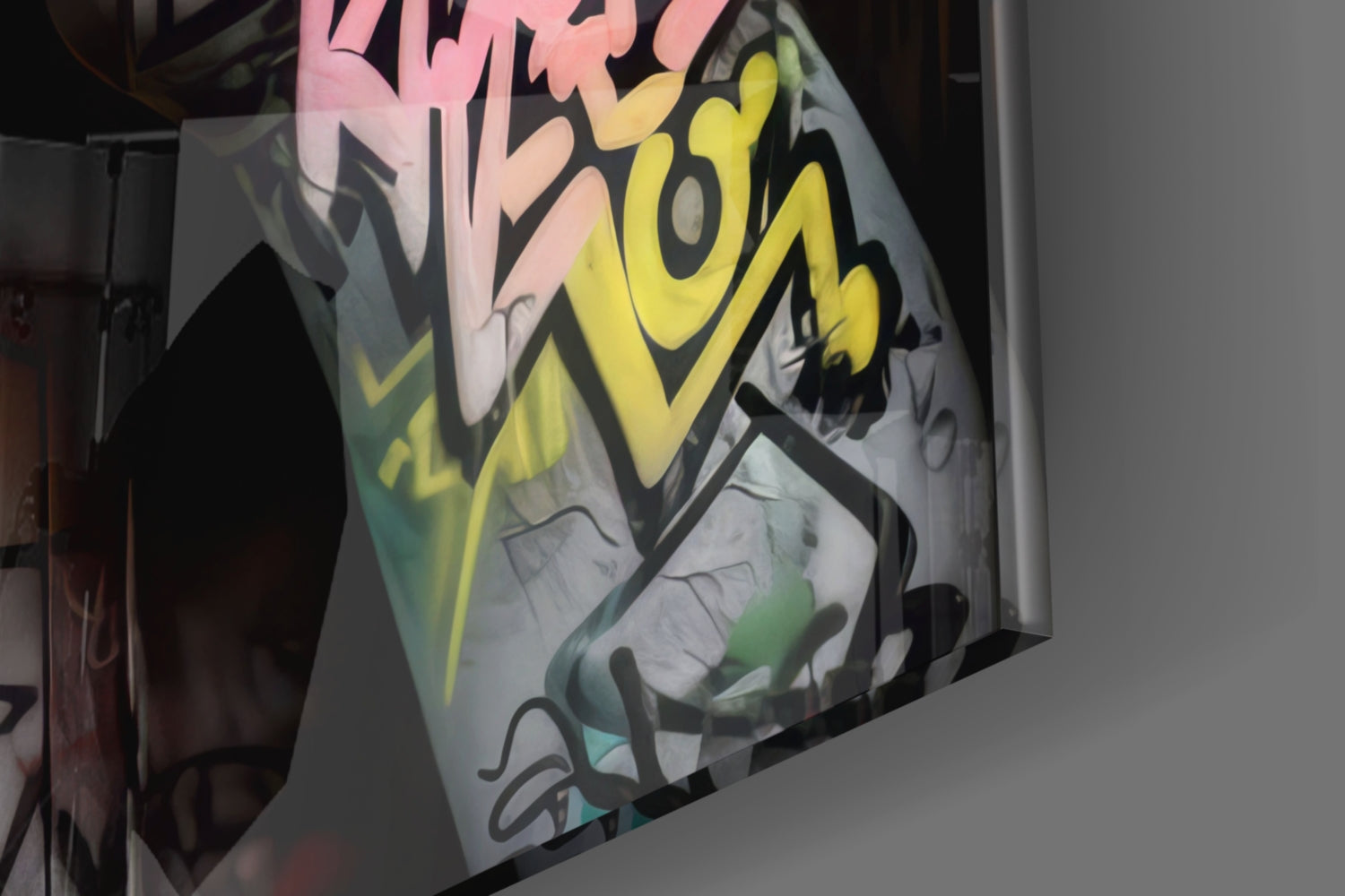 Angled view of glass wall art displaying colorful graffiti-style lettering in pink, yellow, and green with black outlines on white background.