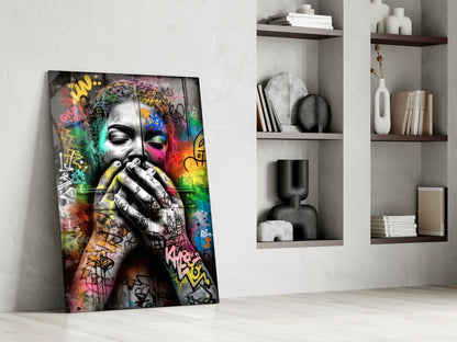 Colorful graffiti street art glass panel leaning against white wall beside minimalist shelving unit with decorative objects and books.