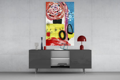 Colorful abstract glass wall art featuring red rose, yellow section, and blue patterns displayed above dark gray media console with red lamp and accessories.