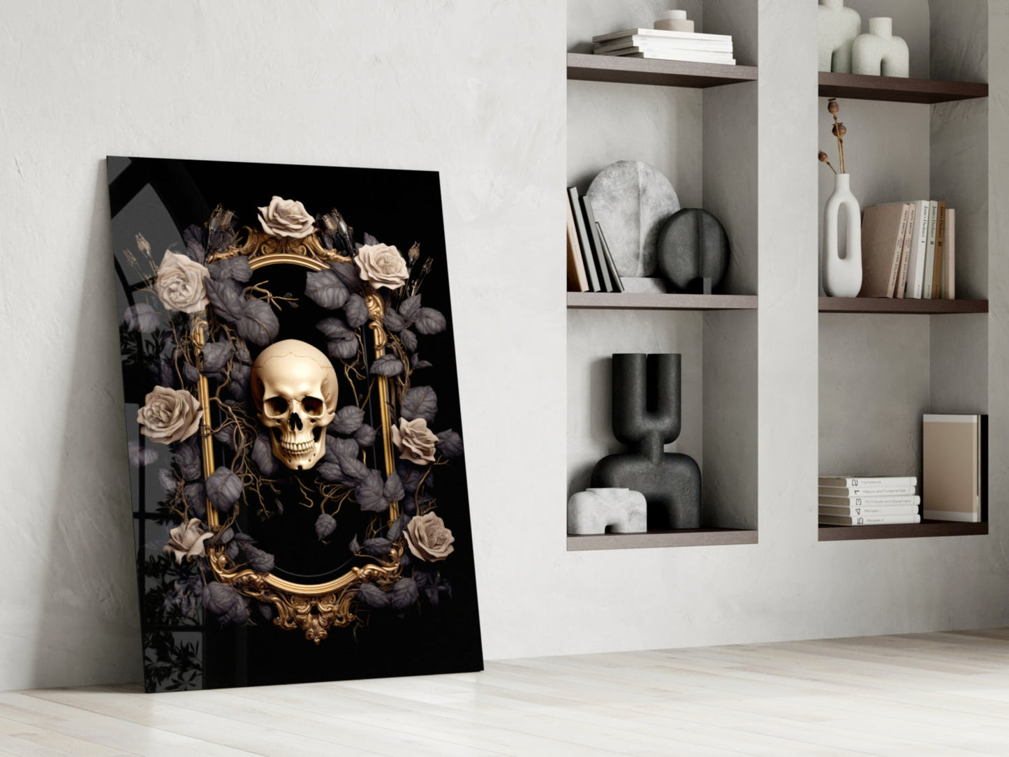 Gold skull framed by cream and charcoal roses on black glass panel leaning against white wall beside shelving.
