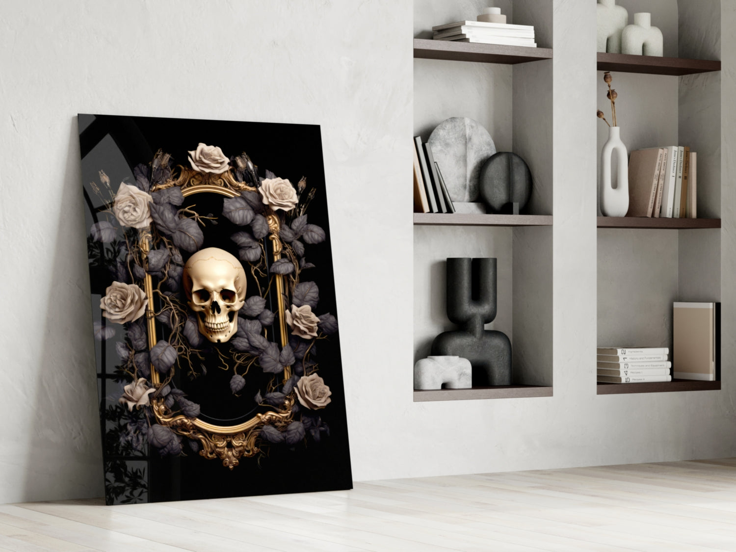 Gold skull framed by cream and charcoal roses on black glass panel leaning against white wall beside shelving.