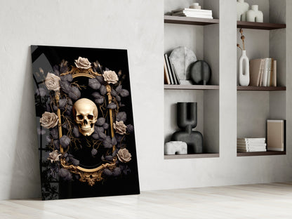 Gold skull framed by cream and charcoal roses on black glass panel leaning against white wall beside shelving.