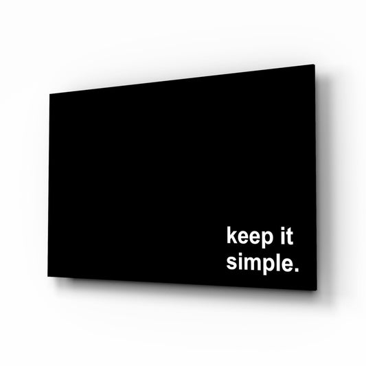 Black glass wall art panel with white text reading "keep it simple." displayed at an angle against white background.