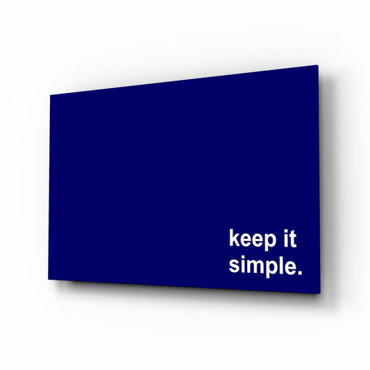 Navy blue tempered glass panel with white "keep it simple." text, photographed at an angled perspective casting a shadow.