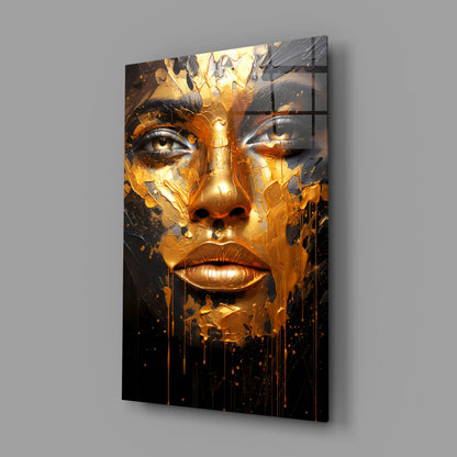 Gold and black glass wall art depicting a stylized face with dripping melted effect, displayed at angle against gray wall.