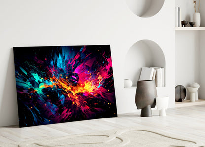 Vibrant glass wall art leaning against white wall displaying explosive cyan, magenta, and yellow abstract burst pattern on black background.