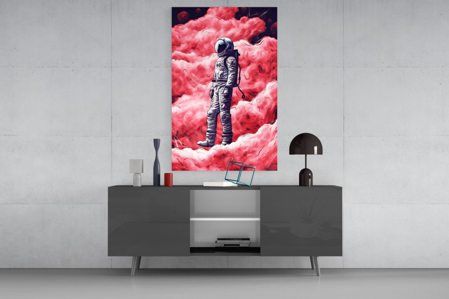 Modern living room display featuring framed glass wall art of an astronaut standing amid pink clouds, mounted above a dark console table with decorative accessories.