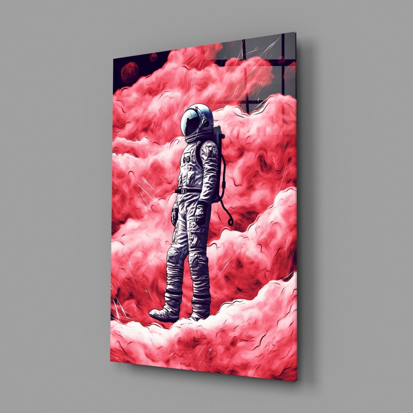 Glass wall art panel displayed at an angle showing a spacesuit figure standing among vivid pink and white clouds against a gray background.