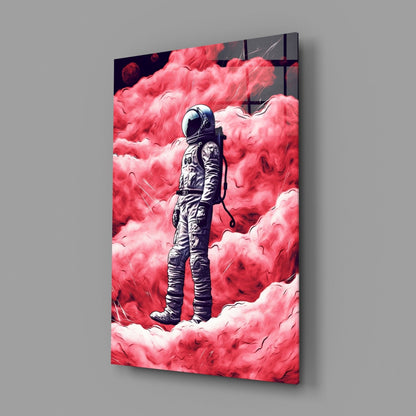 Glass wall art panel displayed at an angle showing a spacesuit figure standing among vivid pink and white clouds against a gray background.
