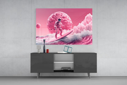 Pink glass wall art depicting an astronaut surfing on waves beneath a textured pink planet, displayed above a dark modern media console.