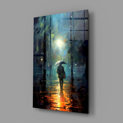 Glass wall art panel displaying a solitary figure with umbrella in a rain-lit urban alley, mounted at an angle against gray wall.