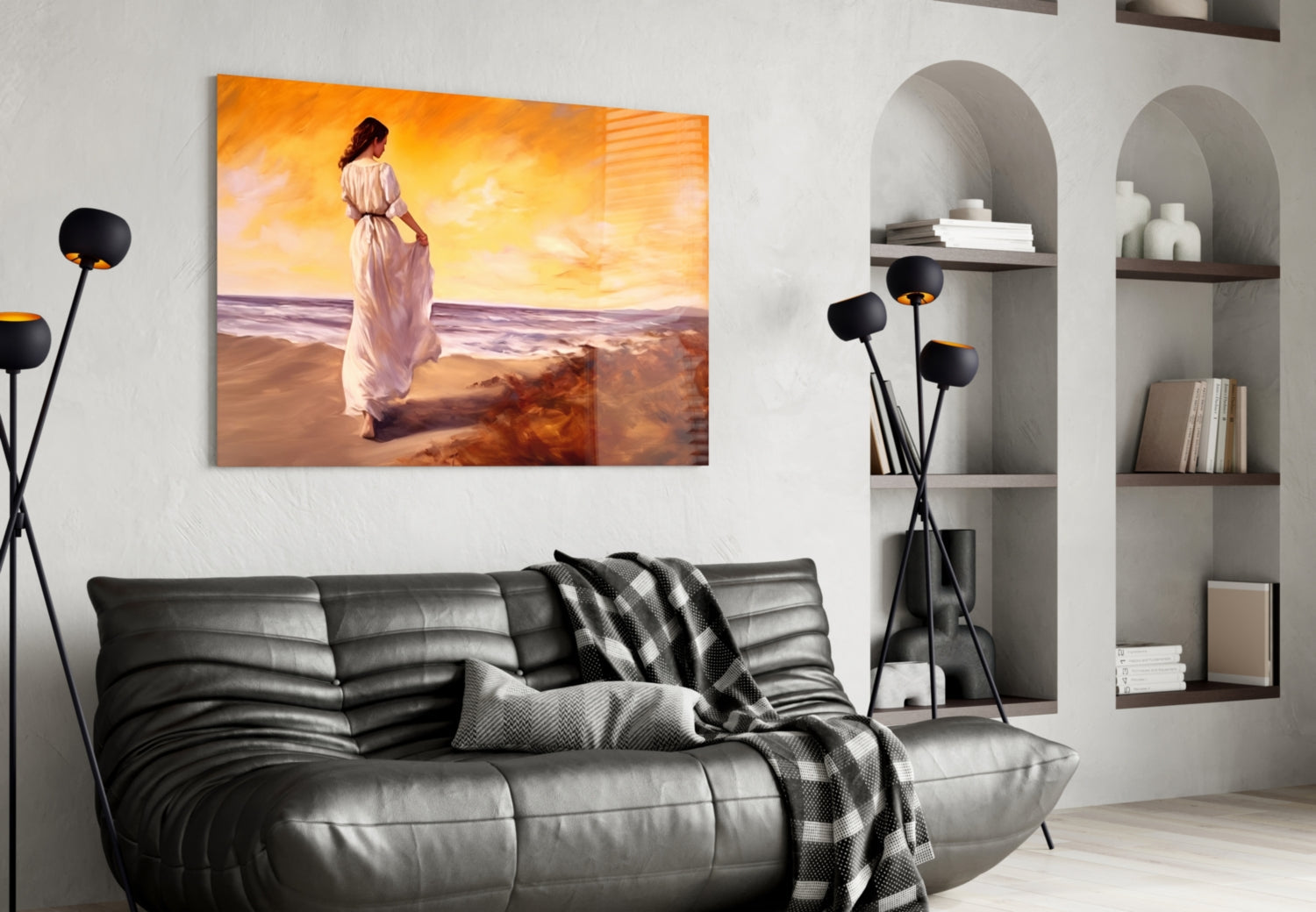 Glass wall art depicting a woman in a white dress standing on a beach at sunset, displayed above a black leather sofa in a modern living room.