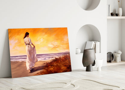 Leaning glass art panel depicting woman in pink dress on sunset beach, displayed in minimalist white interior with decorative objects.