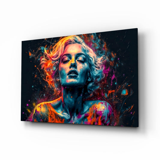 Angled view of glass wall art featuring a colorful portrait of a woman with vibrant neon orange, pink, and blue paint splatters against a dark background.