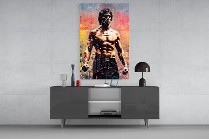 Colorful pop art glass wall panel featuring shirtless muscular man against orange and yellow cityscape backdrop, displayed above modern console table.