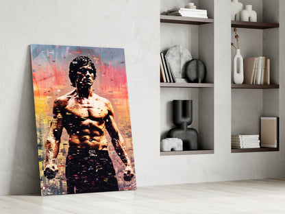 Vibrant glass wall art featuring shirtless man with orange and yellow cityscape overlay, leaning against white wall with wooden shelving.
