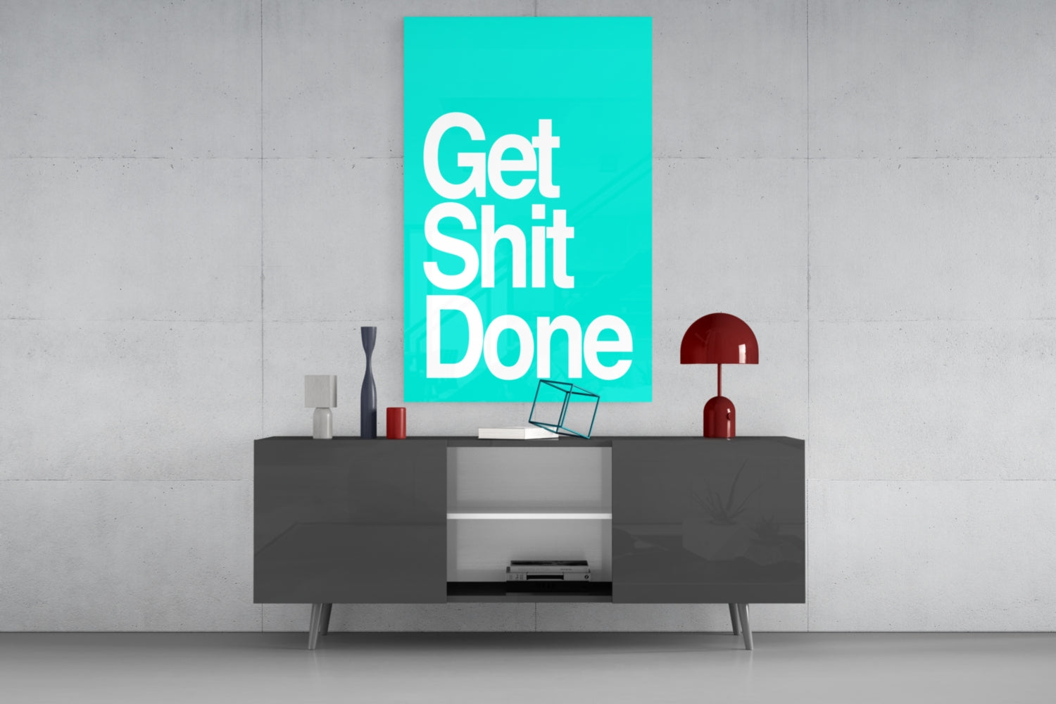 Turquoise glass wall art with "Get Shit Done" text displayed above dark sideboard with decorative objects and lamp.