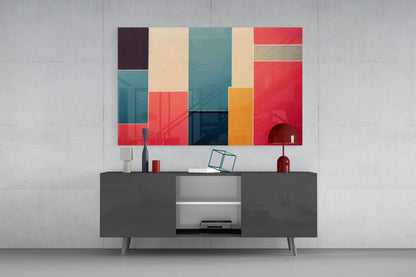 Colorful geometric glass wall art featuring red, teal, cream, and navy rectangles displayed above a dark media console in a modern living room setting.