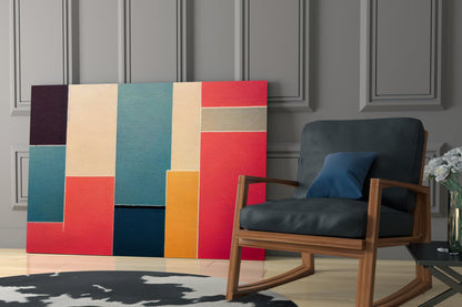 Colorful geometric glass wall art with red, teal, cream, orange, and navy rectangles displayed behind a wooden rocking chair in a modern interior.