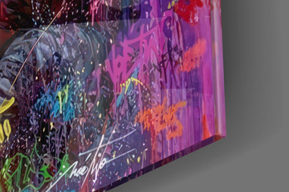Colorful glass wall art panel displaying vibrant purple, pink, orange, yellow, and green abstract graffiti-style design at an angled perspective against gray background.