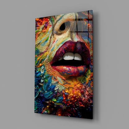 Angled view of glass wall art panel displaying vibrant multicolored textured lips with coral and floral patterns against neutral background.