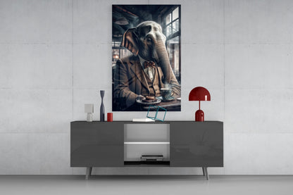 Framed glass wall art depicting an elephant in formal attire seated at a table, displayed above a gray media console in a modern interior setting.