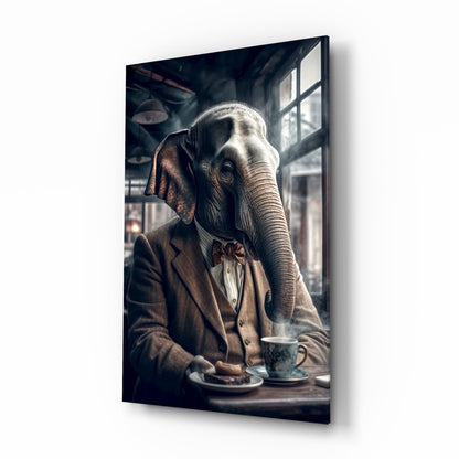 Anthropomorphic elephant in brown blazer and bow tie seated at table with tea cup, viewed at angle showing glass wall art mounted on white background.