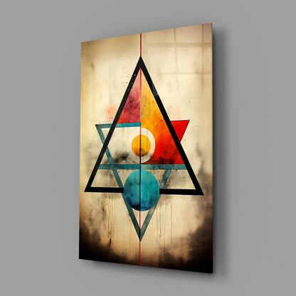 Abstract geometric glass wall art featuring nested triangles in black with colorful interior shapes in red, orange, yellow, and teal on aged beige wood background.