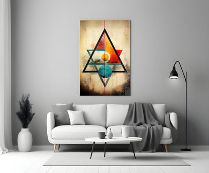 Geometric glass wall art featuring overlapping black triangles with colorful inner shapes in red, orange, yellow, teal, and blue on textured golden background, displayed above white sofa in modern living room.
