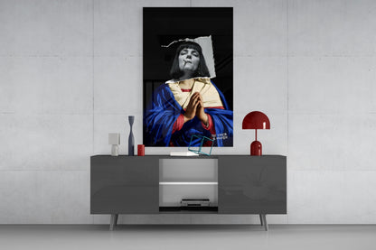 Vertical glass wall art featuring a black and white portrait with hand-colored blue robe and red accents, displayed above a gray media console in a minimalist interior setting.