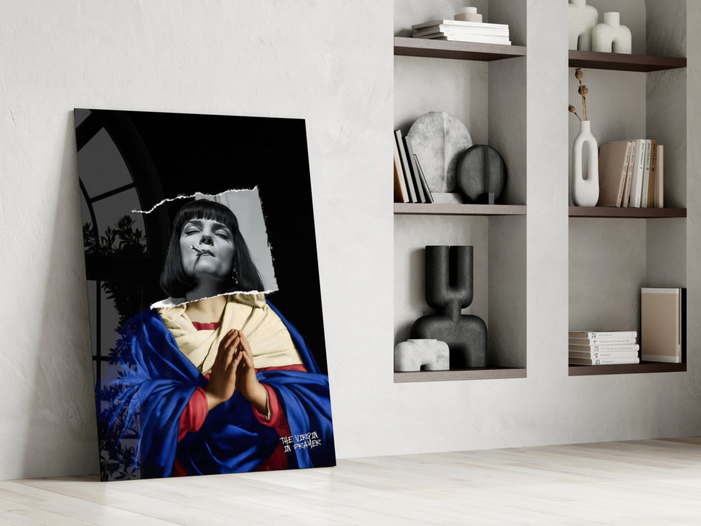 Contemporary glass wall art leaning against white wall displays black and white portrait with blue and gold fabric, beside built-in shelving with decorative objects and books.