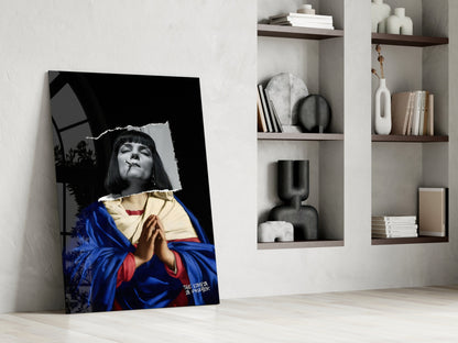Contemporary glass wall art leaning against white wall displays black and white portrait with blue and gold fabric, beside built-in shelving with decorative objects and books.