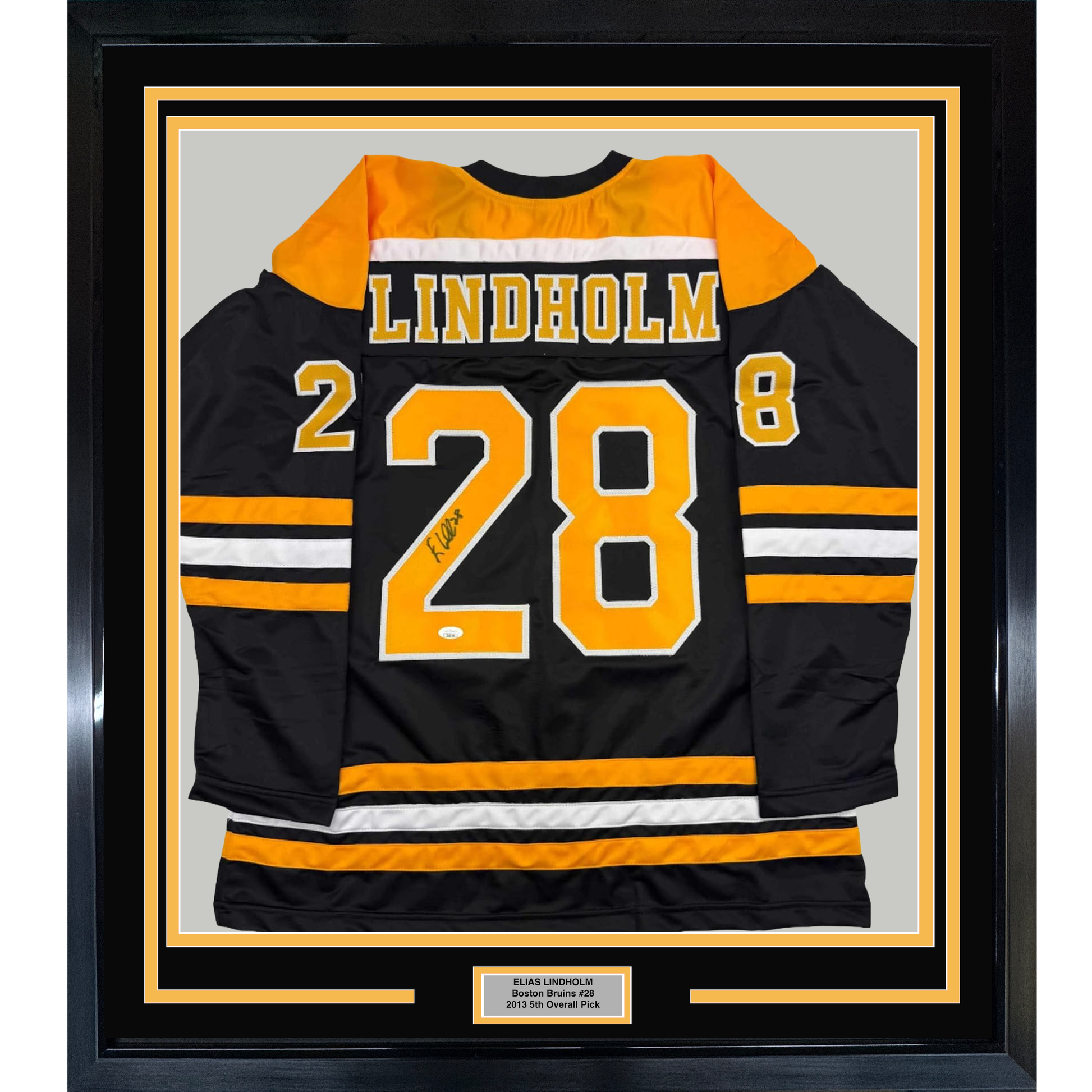 Signed black Boston Bruins hockey jersey number 28 with "Lindholm" name, displayed flat in black frame with yellow borders.