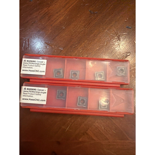 Two red plastic insert cases with cancer warning labels displayed on a wooden surface, showing metallic cutting inserts visible through transparent compartments.