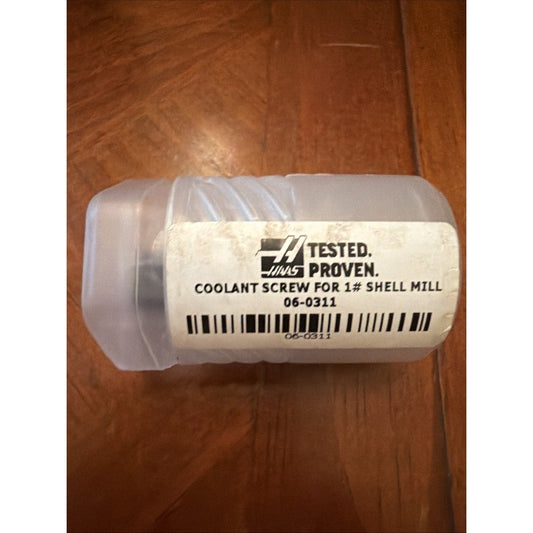 Translucent plastic container with white label reading "TESTED. PROVEN. COOLANT SCREW FOR 1½ SHELL MILL 06-0311" on wooden surface.