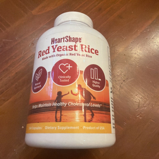 White plastic bottle of HeartShape Red Yeast Rice supplement with red and orange sunset label, displayed on wooden surface.