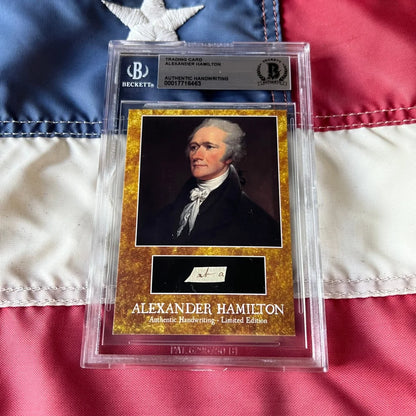 A golden-framed beckett graded alexander hamilton trading card featuring hamilton handwriting and authentic words encased in a slab