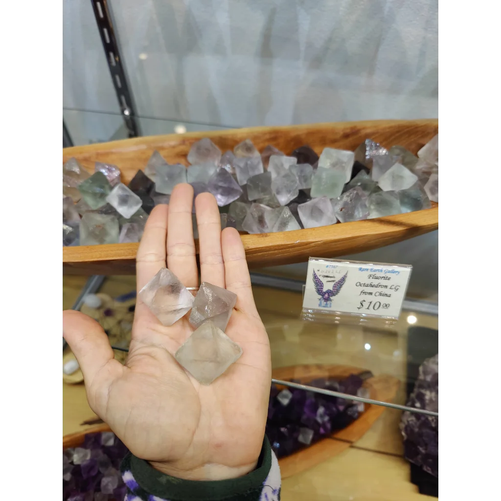 Hand holding large clear faceted fluorite octahedron with purple green hues
