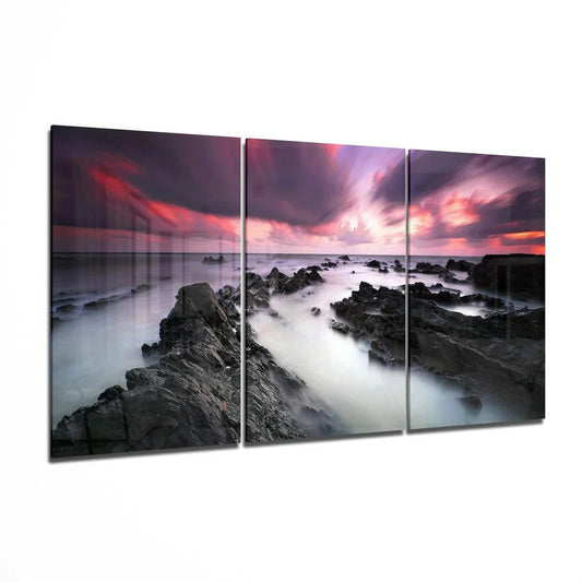 Dramatic coastal sunset glass wall art with purple pink swirls over rocks